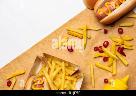 Blick von oben auf die leckere Pommes mit Hot Dogs auf Pergamentpapier isoliert auf weißem Stockfoto