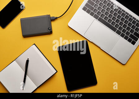 Blick von oben auf die verschiedenen Gadgets mit geöffnet Notebook liegen auf gelbe Oberfläche Stockfoto