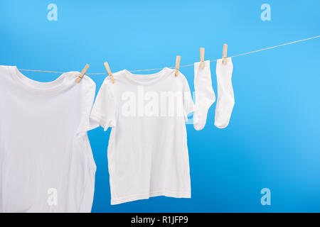 Saubere, weiße T-Shirts und Socken hängen auf wäscheleine isoliert auf Blau Stockfoto