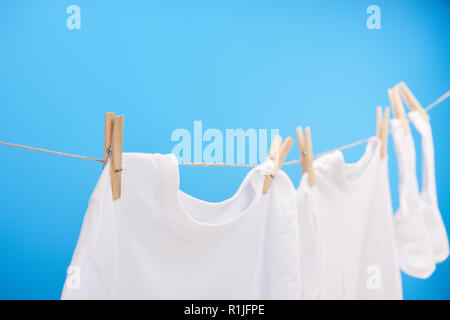 Nahaufnahme eines sauberen weißen T-Shirts und Socken hängen auf wäscheleine isoliert auf Blau Stockfoto