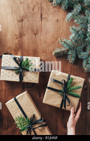 7/8-Ansicht von Frau berühren Geschenkboxen auf hölzernen Hintergrund mit Weihnachtsbaum Niederlassungen Stockfoto