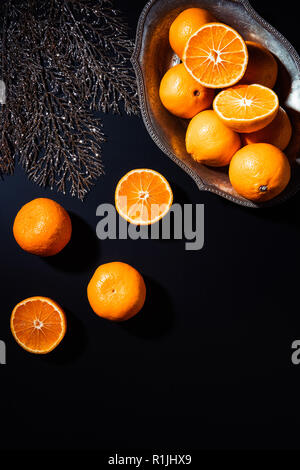 Flach mit Mandarinen, dekorativen silbernen Zweig und Metall Schüssel auf schwarzem Hintergrund Stockfoto