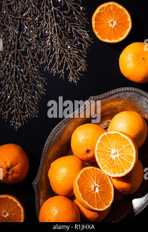 Flach mit Mandarinen, dekorativer Zweig und Metall Schüssel auf schwarzem Hintergrund Stockfoto
