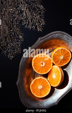 Flach mit Mandarinen in Metall Schüssel und dekorativen silbernen Zweig auf schwarzem Hintergrund Stockfoto