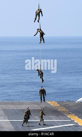 Us-Marines zugeordnet. bis 31 Marine Expeditionary Unit (MEU) von einem MH-60S Sea Hawk Hubschrauber auszusetzen, der "Insel der Ritter" Hubschrauber Meer Combat Squadron (HSC) 25 zugeordnet über dem Flight Deck der Amphibisches Schiff USS Wasp (LHD1) während eine spezielle patrouille Einsetzen/Ausziehen (SPIE) Übung im philippinischen Meer Okt. 11, 2018. Die Wespe, Flaggschiff der Wasp Amphibious Ready Group, mit 31 Marine Expeditionary Unit in Angriff genommen, ist die in der indopazifischen Region Interoperabilität mit Partnern zu verbessern und dienen als ready-Response Force für jede Art von Kontingenz. Stockfoto