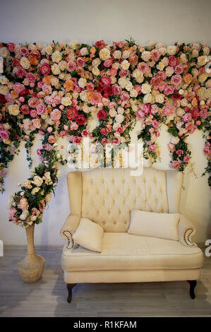 Alte geschnitzte daybed mit weicher Polsterung gegen eine weiße Wand mit rosa Blumen dekoriert. Wunderschöne Girlande. Die Inneneinrichtung ist romantisch, Hochzeit Foto Zone. Stockfoto