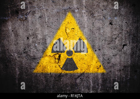 Radioaktiven (Atomkern ionisierende Strahlung) Gefahr Warnung Symbol in dreieckige gelbe Form auf einem massiven gerissenen Beton Zement Wand wit lackiert Stockfoto