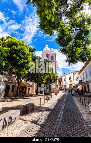 Mit Blick auf die gepflasterte Straße und Kirche in der Stadt Burgau, Algarve, Portugal Stockfoto