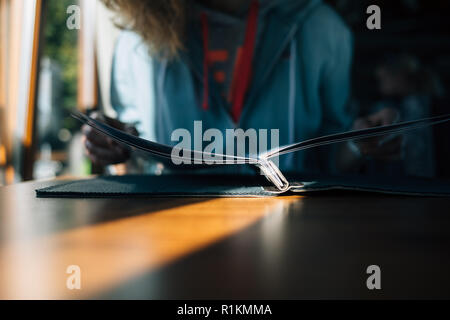 Weibliche legere Kleidung auswählen Gericht an einem sonnigen Tag, close-up. Nicht erkennbare junge Frau zu schlagen durch Menü am Tisch sitzen im Cafe. Stockfoto