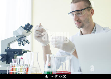 Wissenschaft und runde Konzept, Wissenschaftler testen Rohr und Ablegen von chemischen Reagenzien, junger Mann Erforschung Flüssigkeit im Labor Stockfoto