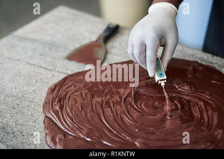Mitarbeiter beobachten die Temperatur der geschmolzene Schokolade auf einem Tisch Stockfoto