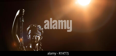 Eine goldene Statue von Lady Gerechtigkeit steht in schwarzen Umgebung. Die Sonne ist mit einer Hintergrundbeleuchtung ausgestattet und produziert Lens Flares. Stockfoto