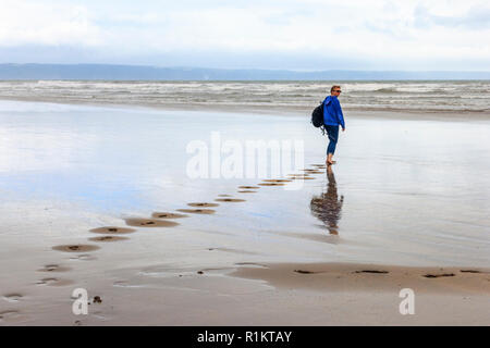 Barfuß Frau in Freizeitkleidung in Richtung Meer auf der windigen Strand bei Westward Ho, Devon, Großbritannien Stockfoto