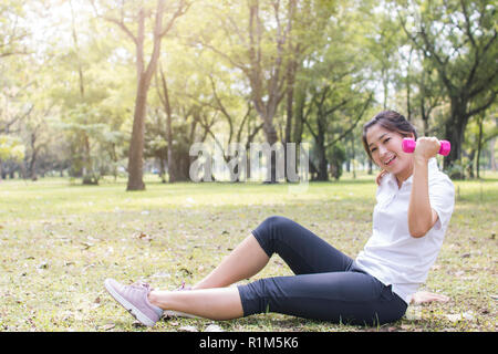 Junge asiatische Frau Wurm bis und mit Rosa Hanteln in park Übung Stockfoto