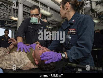 ARABIAN GULF (Okt. 2010) 11, 2018) Hospital Corpsmen 2. Klasse Israel Castro und Alyssa Gupiteo untersuchen simulierten Verletzungen des Marine Corps Sgt. Markieren Mendez, an die 13 Marine Expeditionary Unit (MEU), während einer Messe Unfallversicherung bohren an Bord der Wasp-Klasse amphibisches Schiff USS Essex (LHD2) während der regelmäßigen Bereitstellung mit der Essex Amphibious Ready Group (ARG) und 13 MEU. Essex ist eine tödliche, flexibel, und anhaltende Navy-Marine Corps Team in die USA 5 Flotte Bereich der Maßnahme zur Unterstützung der Marine im Einsatz für die Stabilität und Sicherheit in der Zentrale zu gewährleisten Stockfoto