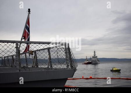 Standing NATO Maritime Group 1 (Snmg 1) Schiff norwegische Fregatte HNoMS Helge Ingstad ruht pierside in Trondheim, Norwegen Oktober 21, 2018 als Schlepper Fraktionskollegen unterstützen, Belgische Fregatte BNS Louise Marie in den Hafen bei einem Port besuchen Sie vor Ausübung Trident Zeitpunkt 2018. Trident Stelle soll sicherstellen, dass die NATO-Streitkräfte bereit sind, jegliche Bedrohung aus jeder Richtung zu reagieren. Trident Zeitpunkt erfolgt in Norwegen und in der Umgebung des nördlichen Atlantiks. Mit mehr als 50.000 Teilnehmern aus 31 Nationen, Trident Zeitpunkt 2018 ist eine der größten Übungen der NATO in den letzten y Stockfoto