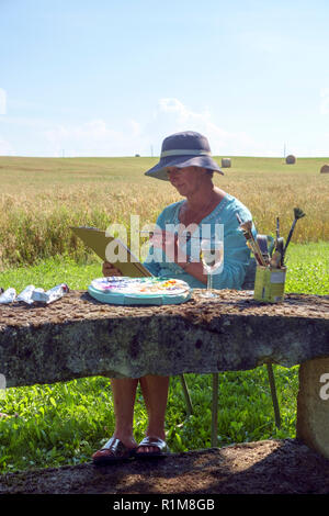 Eine Dame Künstler sitzt am späten Nachmittag Schatten mit einem ländlichen Landschaft arbeiten an der Malerei sie früh in den Tag gestartet. Stockfoto