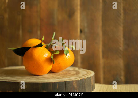 Zweig der drei Orangen Mandarinen mit grünen Blättern liegt auf Holz- sägeschnitt auf alten Holz- Hintergrund. Stockfoto