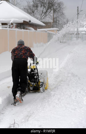 Mann, die Schneefräse Schnee in der Einfahrt zu entfernen. Ein Mann reinigt die Straße vom Schnee. Verschneite Straße. schneereiche Winter Konzept. vertikale Foto. Stockfoto