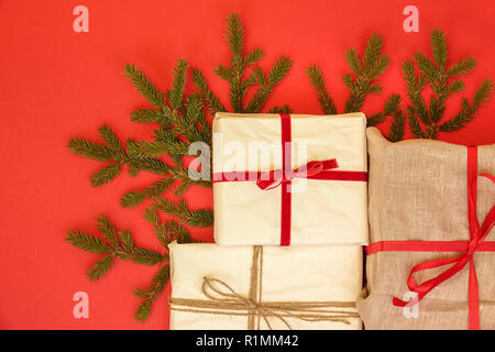 Tanne Ast/Zweig und Weihnachten Geschenkboxen auf rotem Hintergrund. Sackleinen und Wiederverwendung/Recycling Verpackung Papier. Red Ribbon und Leinen string. Stockfoto