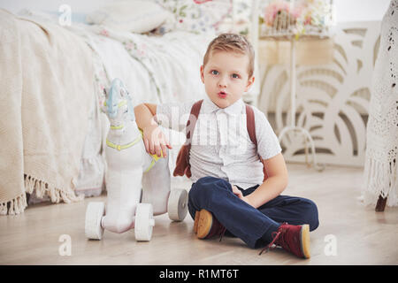 Süße kleine Junge wird zum ersten Mal in die Schule. Kind mit Schultasche und Buch. Kid macht einen Aktenkoffer, Kind im Zimmer auf einem Hintergrund. Zurück zur Schule Stockfoto