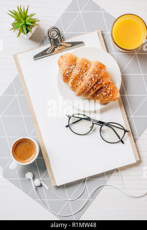 Blick von oben der Brillen, Leere Zwischenablage, Orangensaft, Kaffee und Croissant am Tisch im Büro Stockfoto