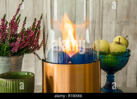 Freistehende portable Glas und Kupfer Metall brennenden Kamin Bio Ethanol Gas auf Holztisch mit T-Stück Schale, blaue Schale mit grünen Äpfeln. Herbst set c Stockfoto