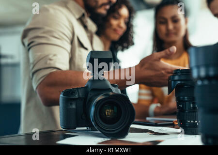 Professionelle DSLR-Kamera und Objektiv auf dem Tisch mit dem Team von Fotografen diskutieren im Hintergrund. Fotograf mit seinem Team während eines phot Stockfoto