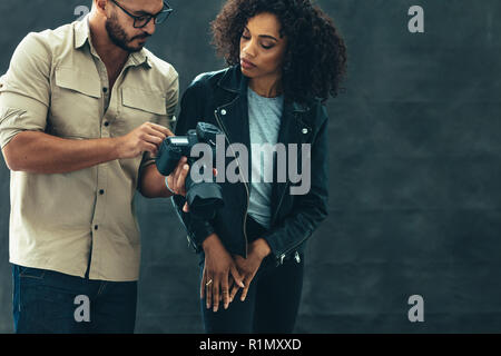 Fotograf sprechen über das Schießen mit dem Modell zeigt das Bild in der Kamera. Studio geschossen von einem Fotografen und einem weiblichen Modell auf einem schwarzen backgroun Stockfoto