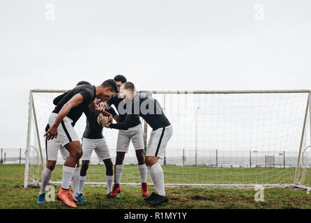 Fußballspieler, die die Hände in einer Gruppe zusammenlegen und eine Pupp-Talk halten. Fußballer, die sich aufmuntern, in einer Huddle auf dem Spielfeld zu stehen. Stockfoto