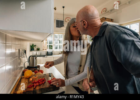 Älterer Mann seine Frau in der Küche zu Hause zu küssen. Mann und Frau Spaß zu haben, während das gemeinsame Kochen in der Küche. Stockfoto