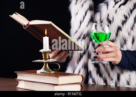 Frau mit Absinth grüne Getränk im Glas lesen Buch. Kerze im Leuchter brennen auf dem Schreibtisch. Mystic und Magie Konzept Bild Stockfoto