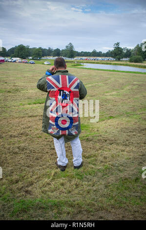 Scooter Enthusiast und Mod im Parka mit aufgenähtem Abzeichen für die WHO und die Union Flag auf seinem Handy an der Stanford Hall, Leicestershire Stockfoto