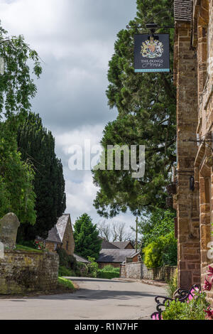 Der von Bäumen gesäumte Hauptstraße im Sommer durch das malerische Dorf Farthingstone, Northamptonshire, Großbritannien Stockfoto