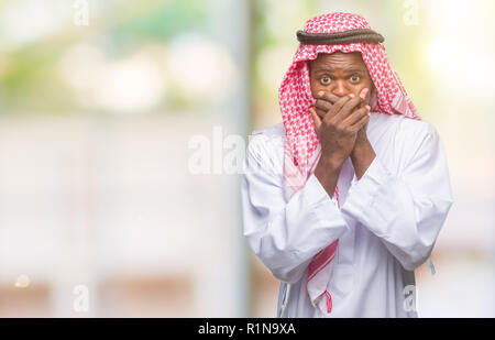 Junge arabische afrikanischen Mann mit traditionellen Kufiya über isolierte Hintergrund schockiert über den Mund mit Händen für Fehler. Geheime Konzept. Stockfoto