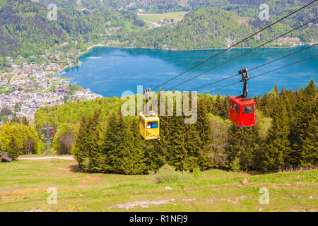 Gelbe und rote Gondeln der Seilbahn Zwoelferhorn (Seilbahn) Reisen nach oben und unten alpine Peak mit einem Blick auf den Ort St. Gilgen und den Wolfgangsee See, Sal Stockfoto