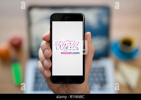 Ein Mann schaut auf seinem iPhone die zeigt die Wizzair logo, während saß an seinem Computer Schreibtisch (nur redaktionelle Nutzung). Stockfoto