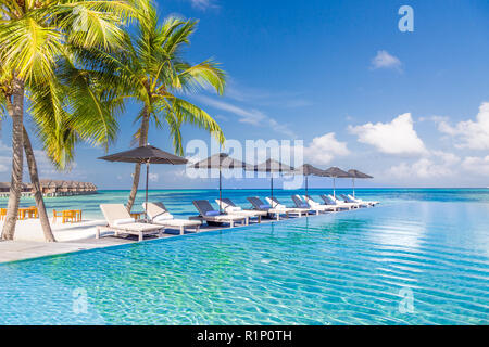 Liegestühle und Infinity Pool über fantastische tropische Lagune. Luxus und Urlaub Konzept Stockfoto
