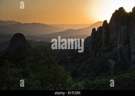 Die riesigen Felsen mit den Klöstern und Sonnenuntergang hinter die Berge in der Ferne in Meteora, Thessalien, Griechenland Stockfoto