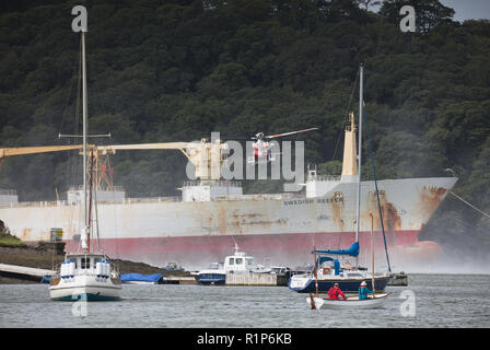 Küstenwache schwebenden Hubschrauber über dem Tanker und ein Hubschrauber Crewmitglied down Winched wird der Unfall zu helfen. River Fal, Cornwall. Stockfoto