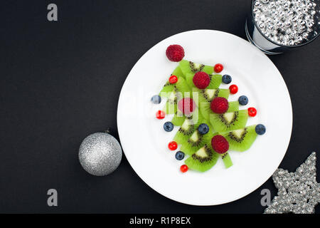 Genießbare Weihnachtsbaum von Kiwi Slices auf einer schwarzen Platte über Dunkle Schiefer, Stein oder Beton Hintergrund Stockfoto