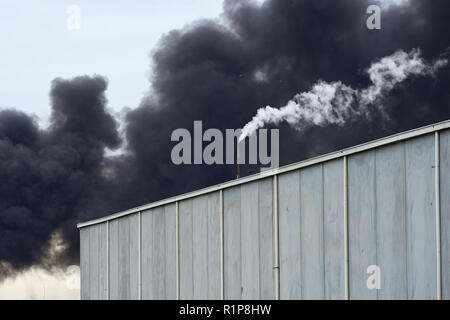 Giftiger Rauch von einem Westen Footscray Brand am 30. August 2018 können gesehen werden brüllend hinter eine moderne Lagerhalle mit kontrastierenden weißen Dampf. Stockfoto