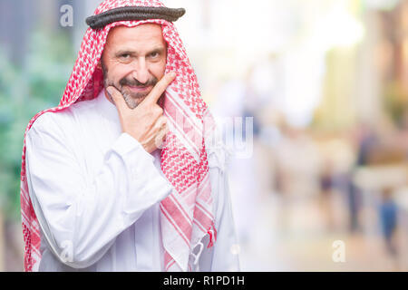 Senior arabischen Mann mit kufiya über isolierte Hintergrund in die Kamera schaut zuversichtlich mit Smile mit verschränkten Armen und Hand am Kinn angehoben. Thinki Stockfoto
