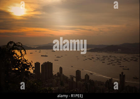 Sonnenuntergang über den Hafen von Hong Kong aus klitsch Lookout, Victoria Peak. Strahlend orange Sonne über entfernte Inseln mit Stadt Hochhäusern im Vordergrund. Stockfoto