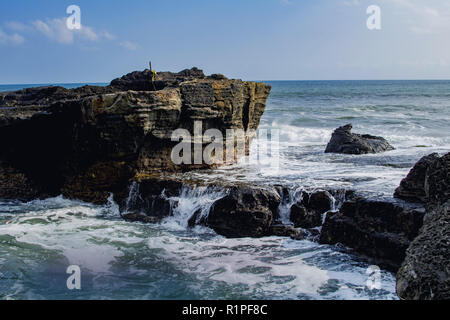 Wasser und Felsen. Leistungsstark. Wellen auf einem felsigen Strand. Hohe Klippe über dem Meer, Sommer Hintergrund, vielen plätschernden Wellen und Stein, sonnigen Tag Stockfoto