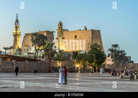 Die Menschen auf dem Platz stehen mit ihren Handys vor den illuminierten Luxor-Tempel bei Nacht mit blauen Himmel und strahlenden alten brickwalls, Luxor Stockfoto