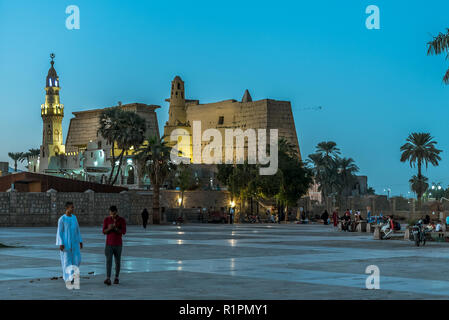 Menschen zu Fuß auf dem Platz vor der alten illuminierten Luxor-Tempel bei Nacht mit dunkelblauen Himmel und glühende brickwalls, Luxor, Ägypten, octob Stockfoto