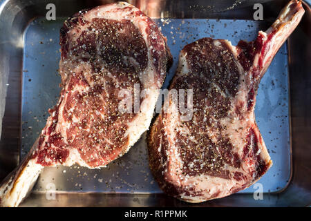 Marinieren schöne Marmorierung abgehangenes Rindfleisch mit Knochen ribeye Steaks mit Salz und Pfeffer Stockfoto