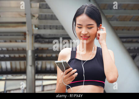 Cute Asien Frau Wasser trinken nach workoutBeautiful Asien Frauen hören die Musik vom Smartphone beim Ausführen Stockfoto