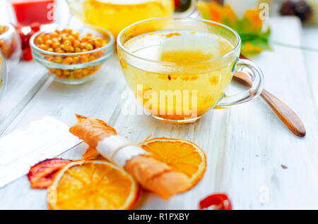 Sanddorn Tee im Glas Tasse und Kännchen und viele verschiedene Obst pastille und Chips auf Frühstück auf weiße Holztisch, Tageslicht, selektive Fokus Stockfoto